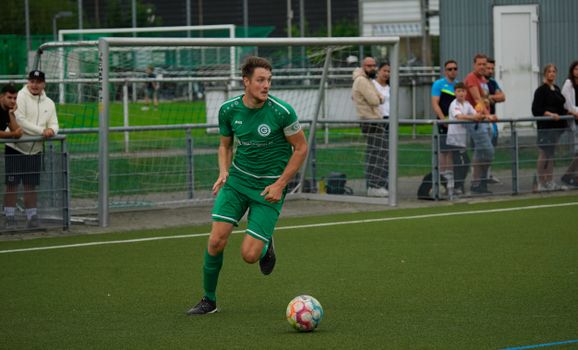 Transfernieuws in Tiel op een smartphone, met voetbalfans bij een regionaal sportpark op de achtergrond